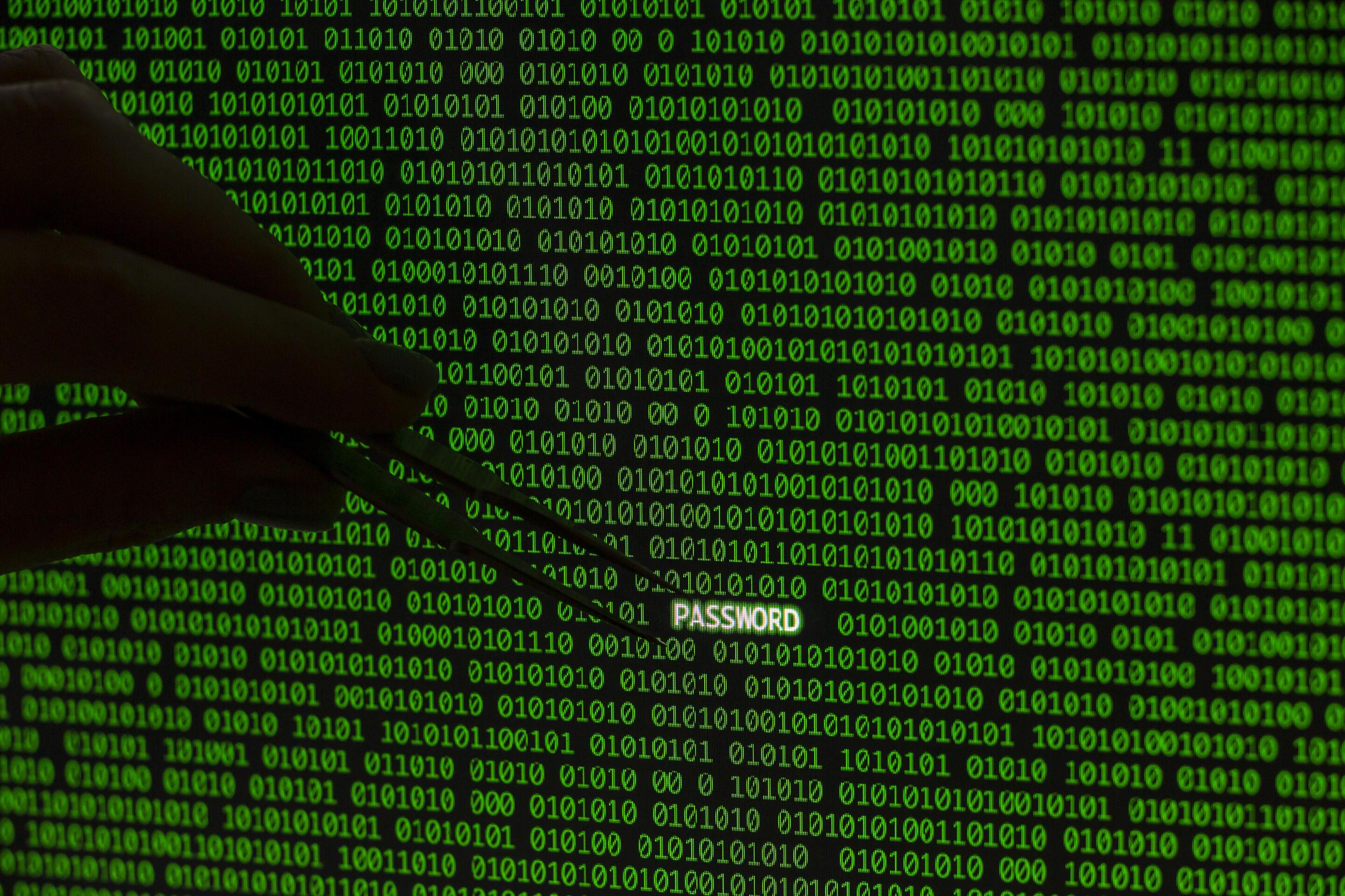 Hand using tweezers to extract the word 'PASSWORD' from green binary code, symbolizing cybersecurity risks and data vulnerabilities.
